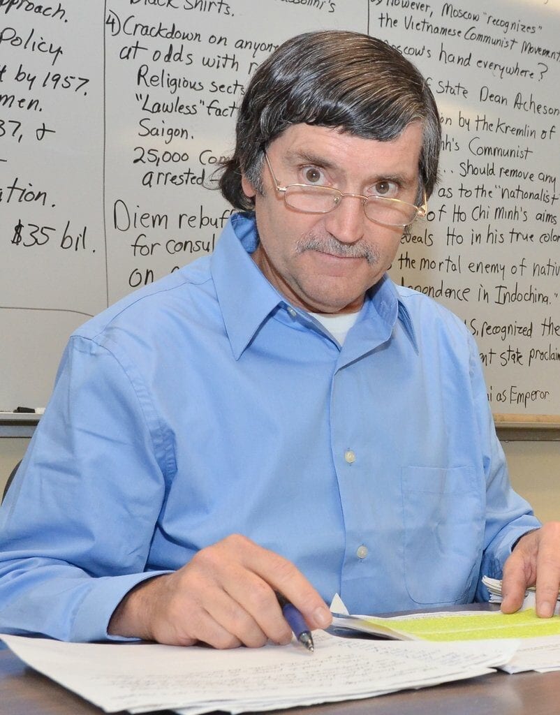 Teacher at desk marking papers with whiteboard notes